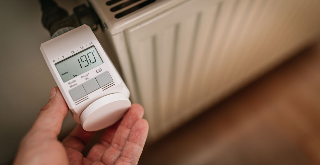 Main ajustant un thermostat numérique moderne affichant 19°C sur un mur blanc dans un intérieur contemporain